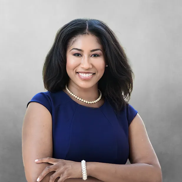 Smiling woman in a blue dress with arms crossed against a gray background.
