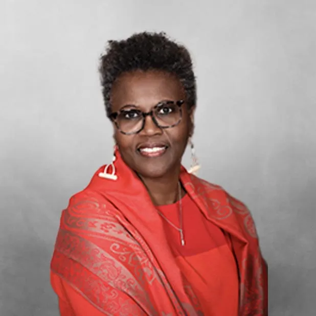 Elegant woman in glasses, red shawl, and earrings, smiling against a gray background.