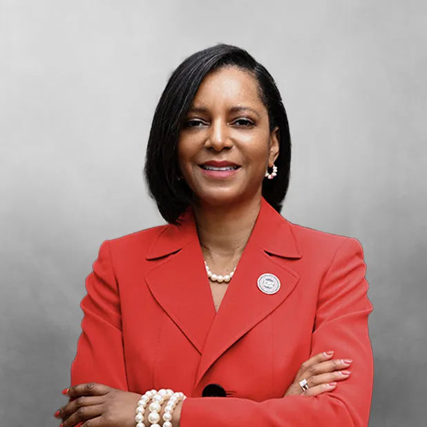 Smiling woman in a red suit with pearl jewelry, arms crossed.