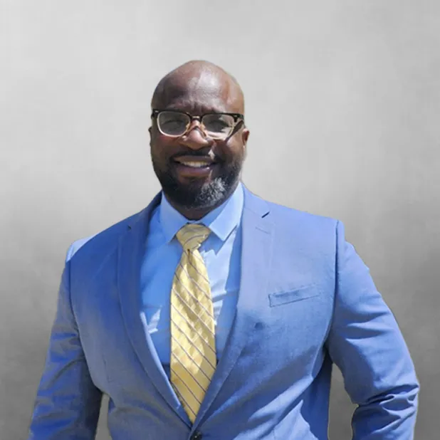 Man in blue suit and yellow tie smiling against a gray background.