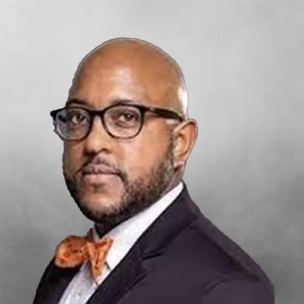 Bald man in glasses wearing a suit and orange bow tie against a gray background.