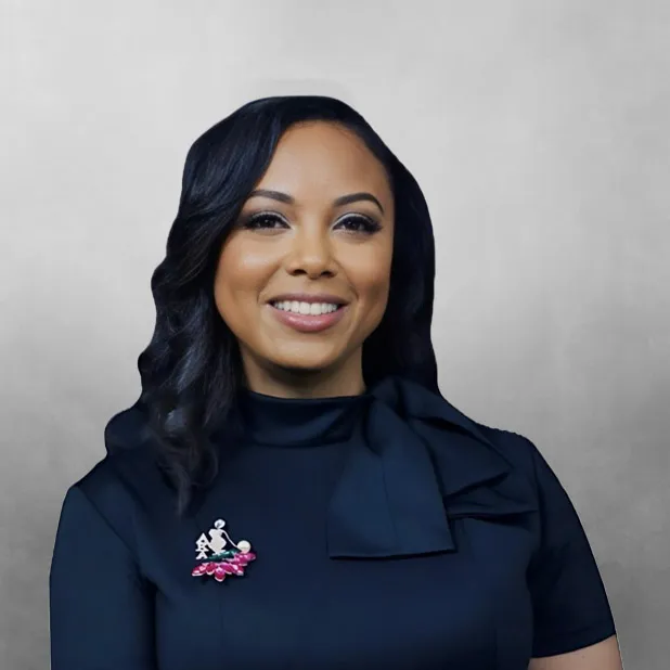Smiling woman with dark hair in a blue dress with a brooch.