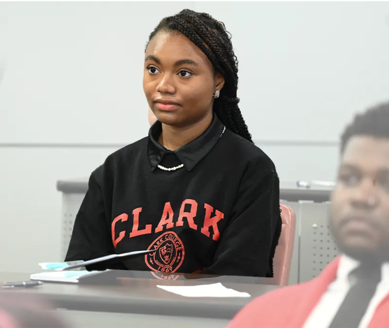 Student sits attentively in a classroom wearing a black "Clark" sweatshirt.