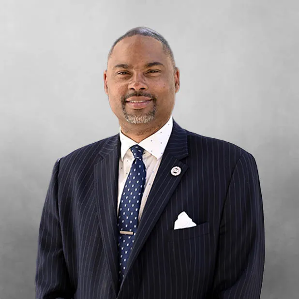 Man in a pinstripe suit and tie against a gray background, smiling.