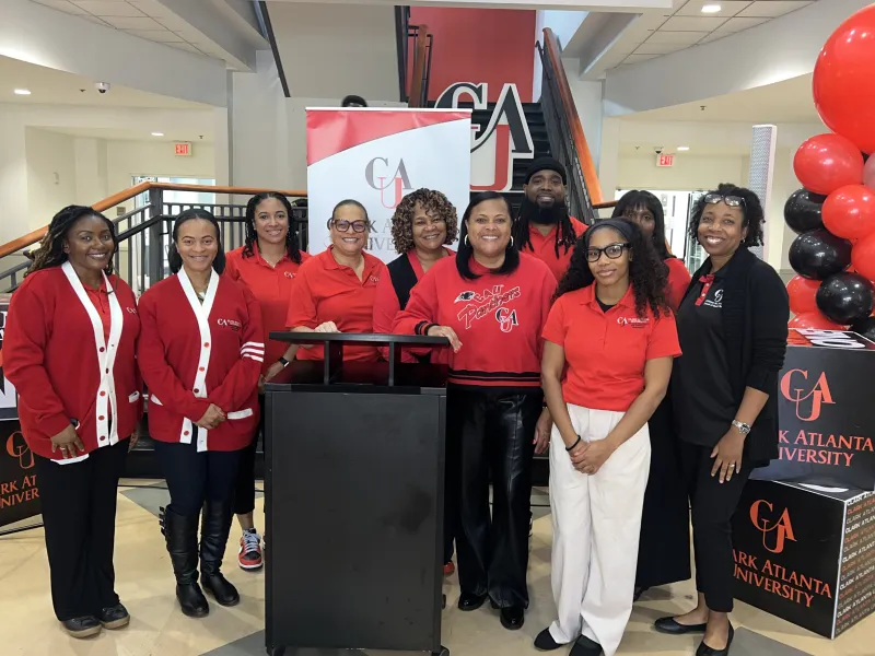 Group of people standing together indoors near a podium, wearing matching red and black outfits.