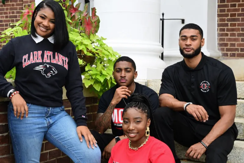 Four students smiling outside a building, with greenery in the background.