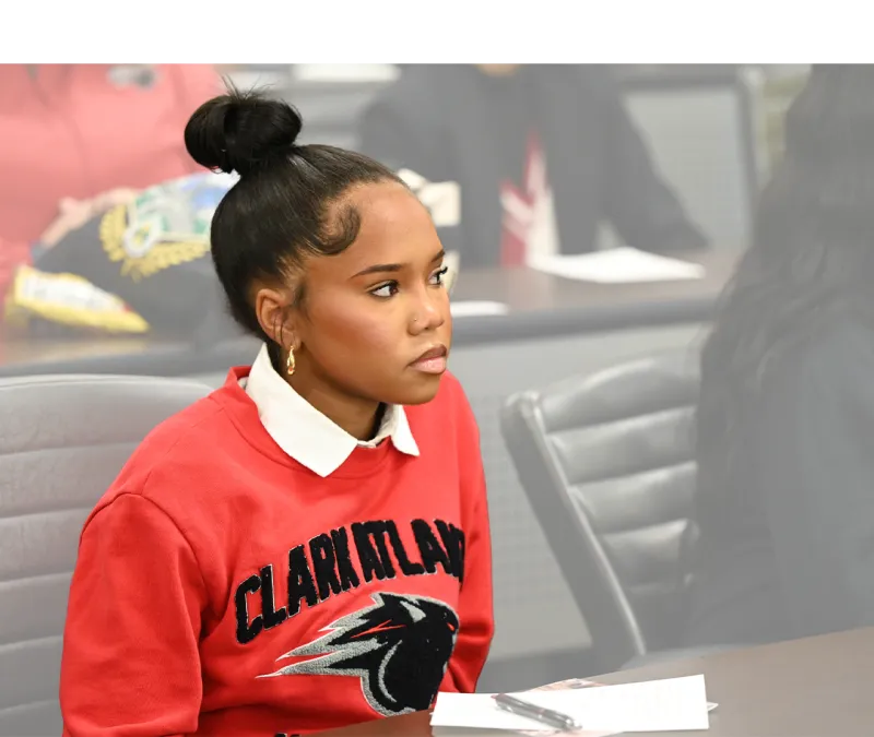 Young woman in a red Clark Atlanta shirt attentively listening in a classroom.