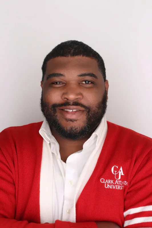 Smiling man in red sweater with white shirt against plain background.
