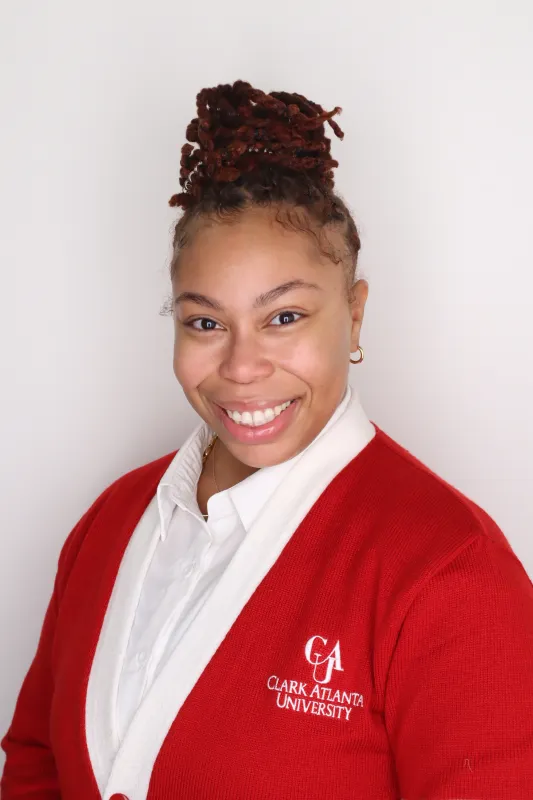 Smiling person in a red cardigan with logo, white shirt, neutral background.