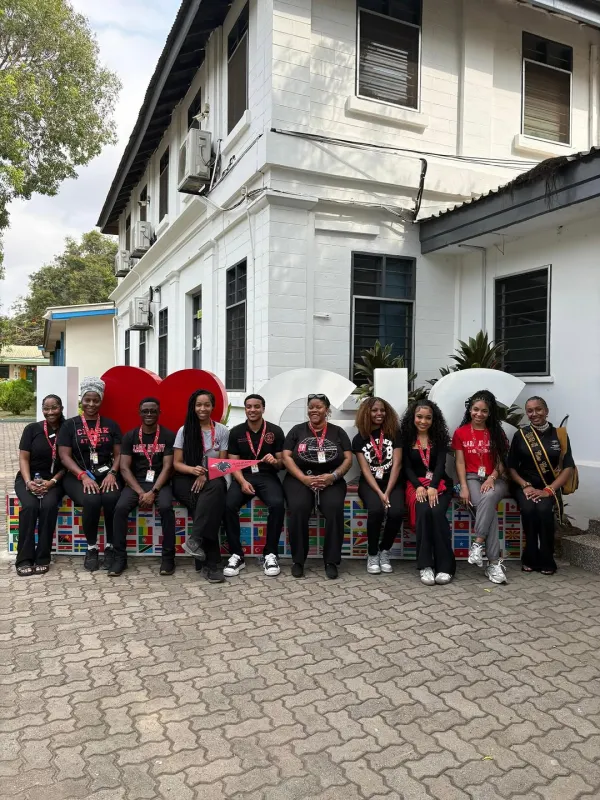 Group of CAU students in black outfits sitting on a bench outside a white building in Ghana.