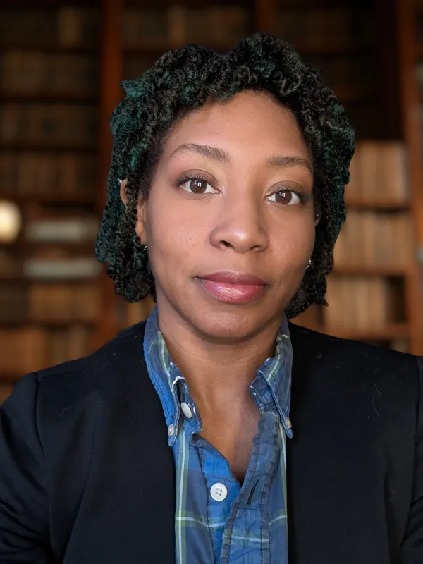 Woman in a library, wearing a blue shirt and dark blazer.