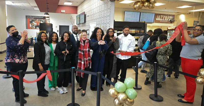 People gathered, cutting a red ribbon in a bakery shop opening event.