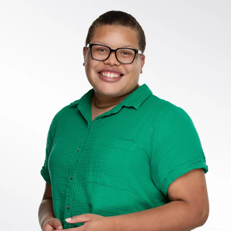 Smiling person in a green shirt and glasses on a light background.