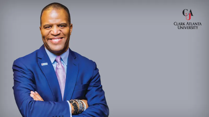 Smiling man in a blue suit with arms crossed, Claflin University logo.