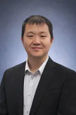 Smiling person in a suit against a blue gradient background, portrait photo.