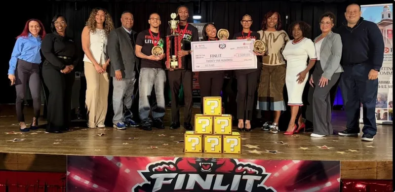 A group of people on stage holding a large check and trophies, with a colorful banner below.