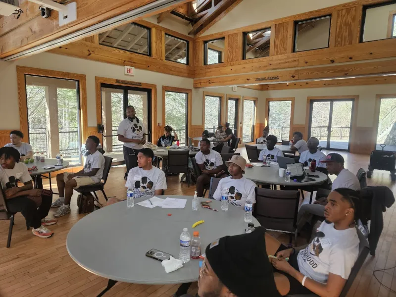 People in a meeting room, seated at round tables, wearing white shirts.