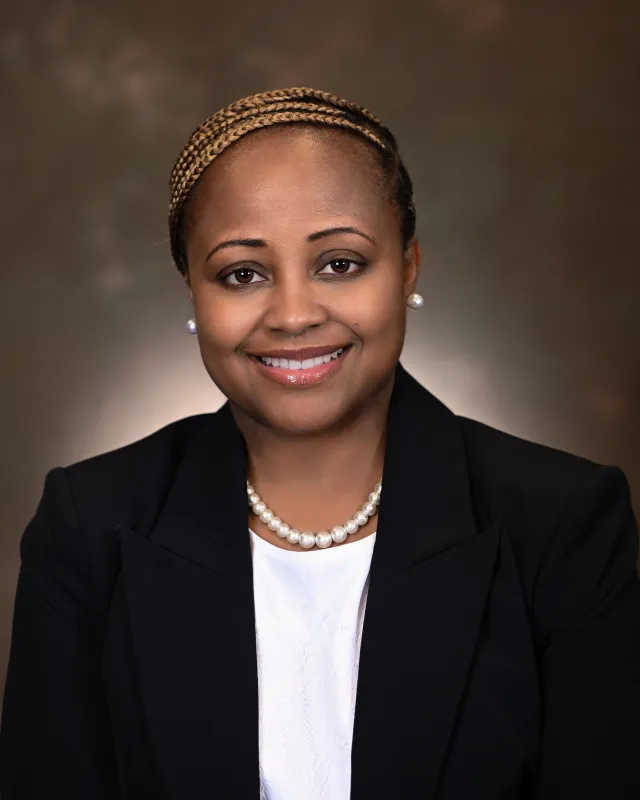 Smiling person in a dark suit with braided hair.