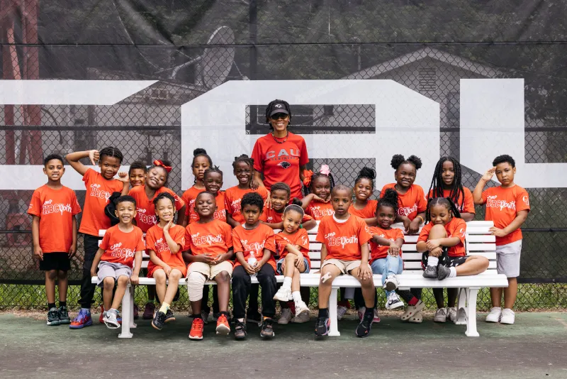 Group of children in red shirts sitting on a bench outdoors.