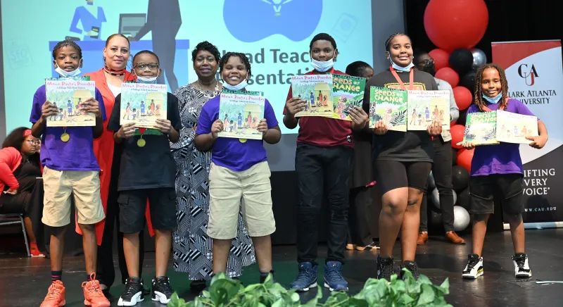 Group of seven people smiling, children holding books with medals on stage.