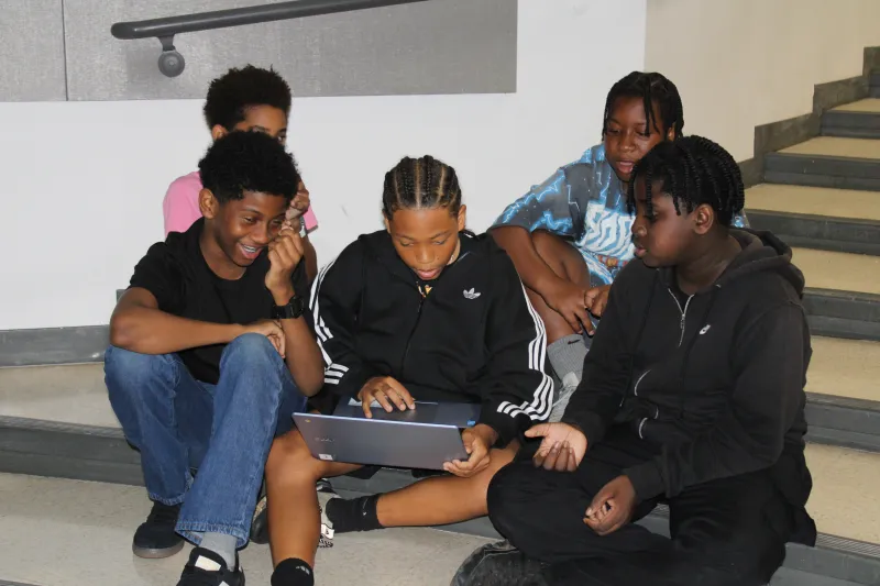 Children sitting on stairs, engaged with a laptop.