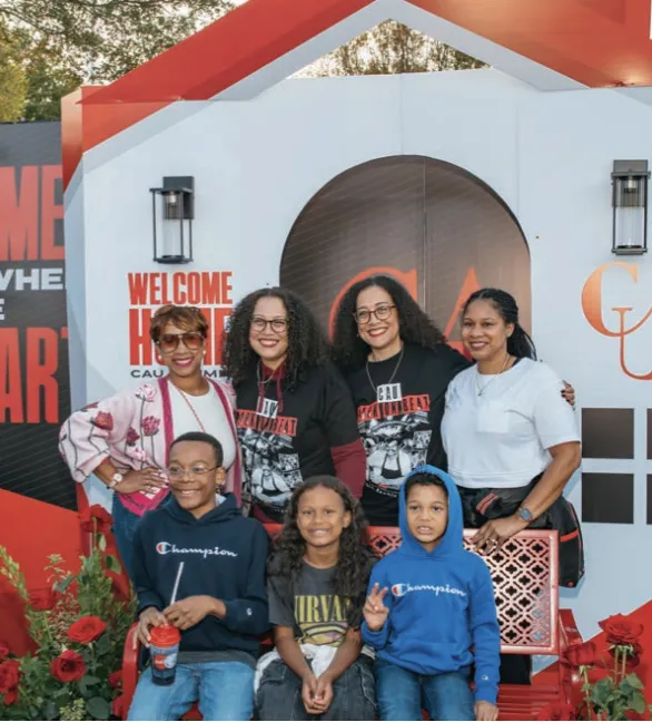 Family smiling in front of a house-shaped backdrop with welcome signs.