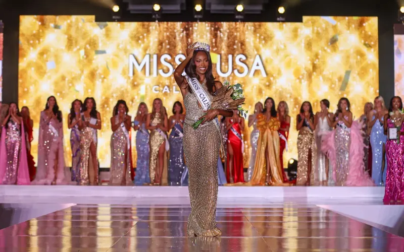 Winner in gown and crown with bouquet on stage, contestants behind her.